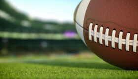 American football ball on grass of football arena, 3d illustration